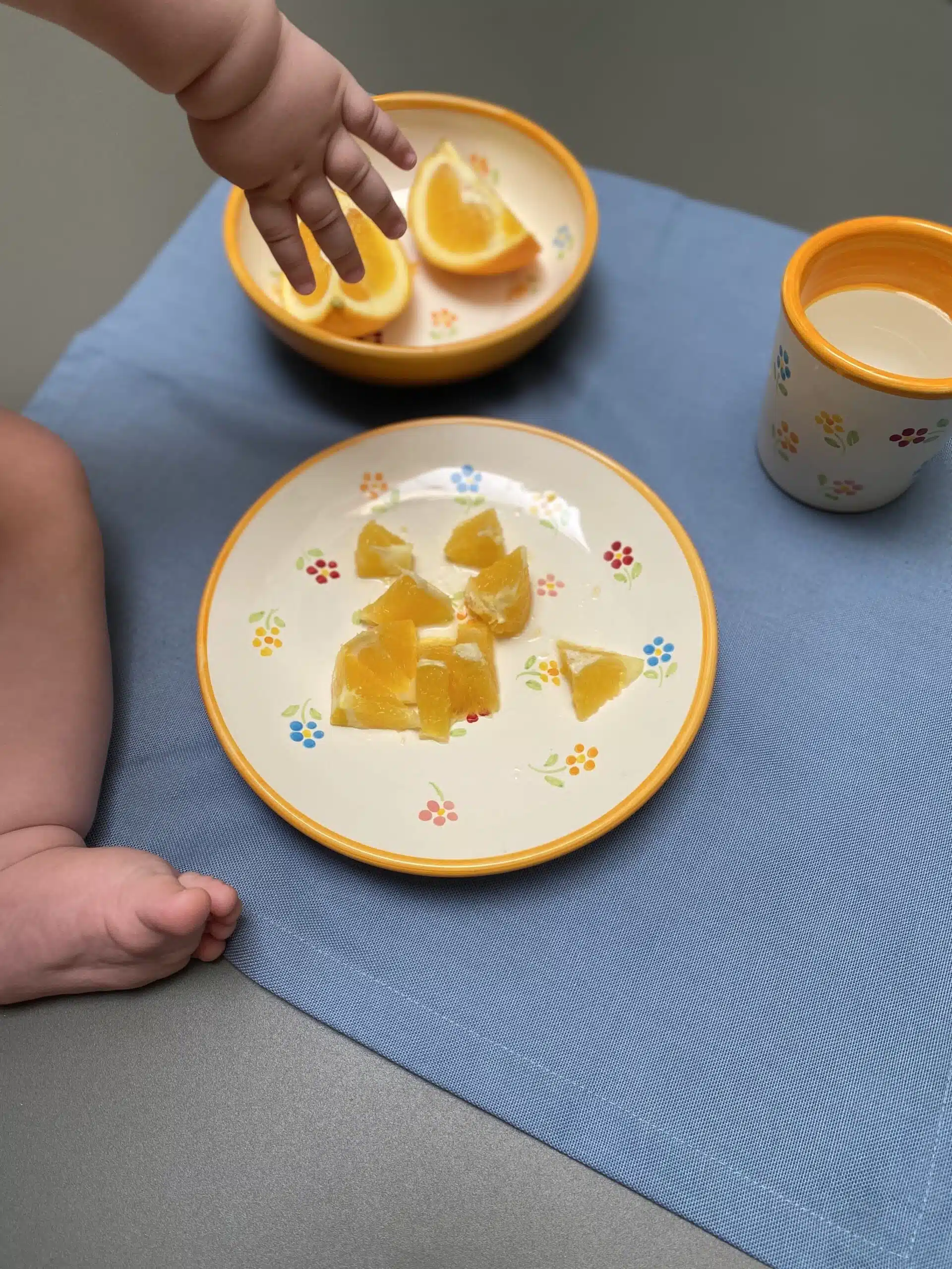 Plato pequeño con gajos de naranja y una mano y pie de un bebé